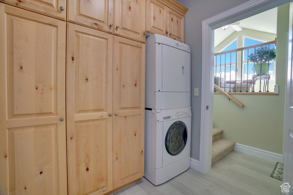 Washroom with cabinets, light tile floors, and stacked washer and dryer