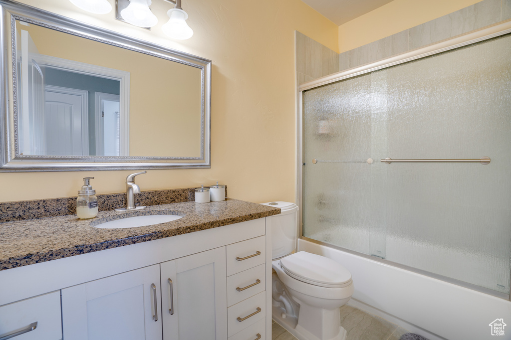 Full bathroom featuring bath / shower combo with glass door, tile floors, toilet, and vanity