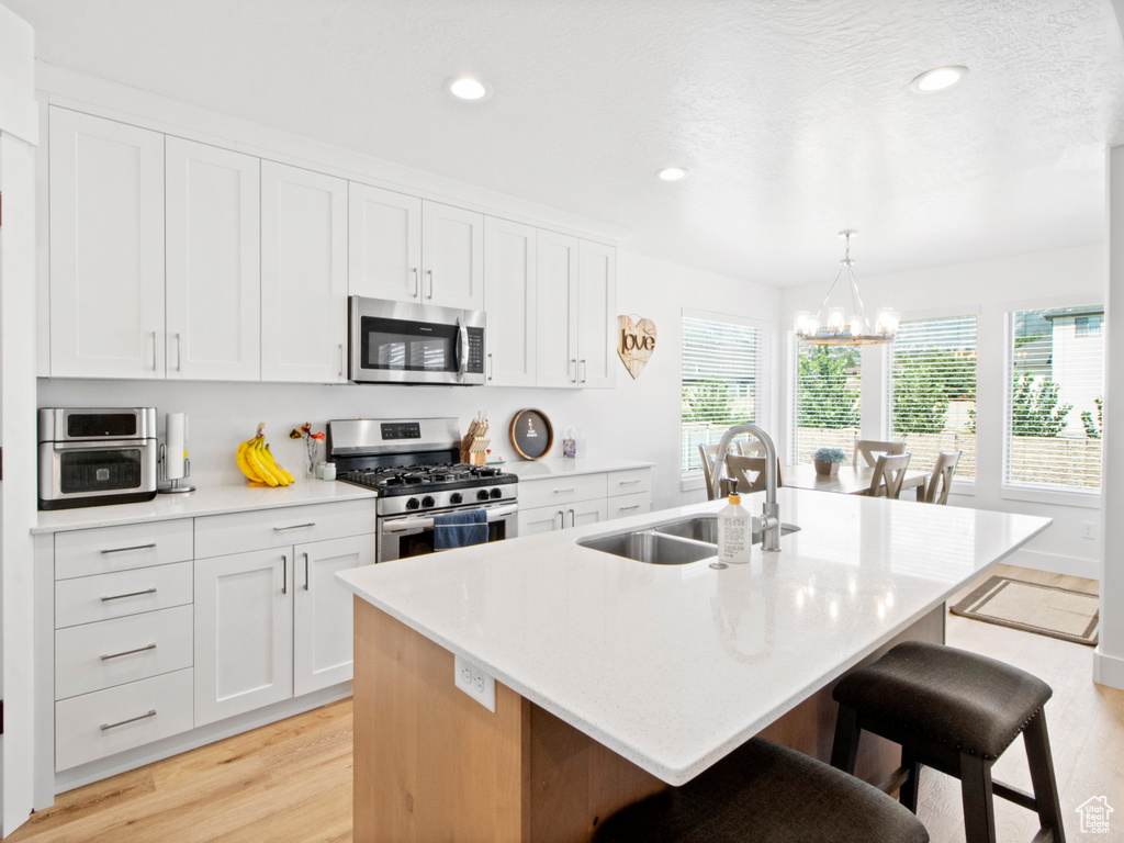 Kitchen featuring sink, appliances with stainless steel finishes, light wood-type flooring, a kitchen breakfast bar, and an inviting chandelier
