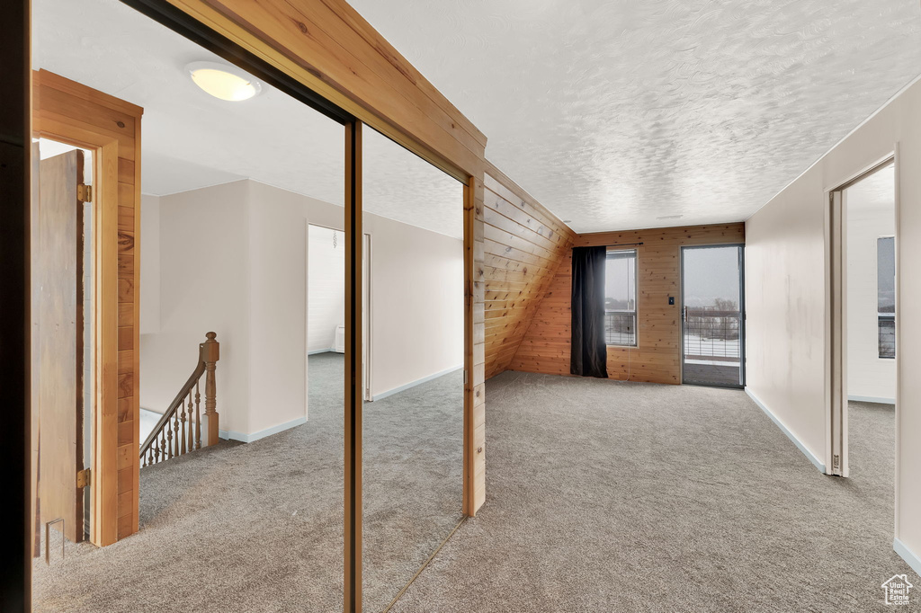 Carpeted spare room featuring wooden walls and a textured ceiling