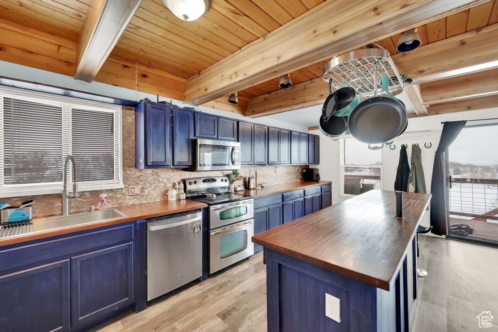 Kitchen featuring appliances with stainless steel finishes, blue cabinetry, beam ceiling, light hardwood / wood-style flooring, and butcher block countertops