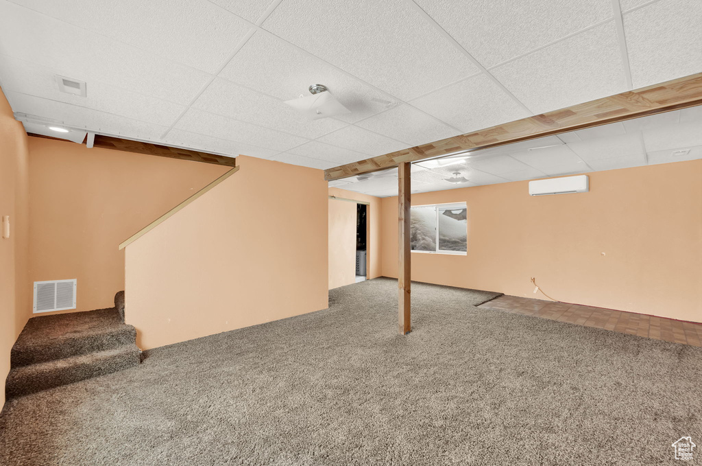Basement featuring carpet floors, a wall mounted AC, and a drop ceiling