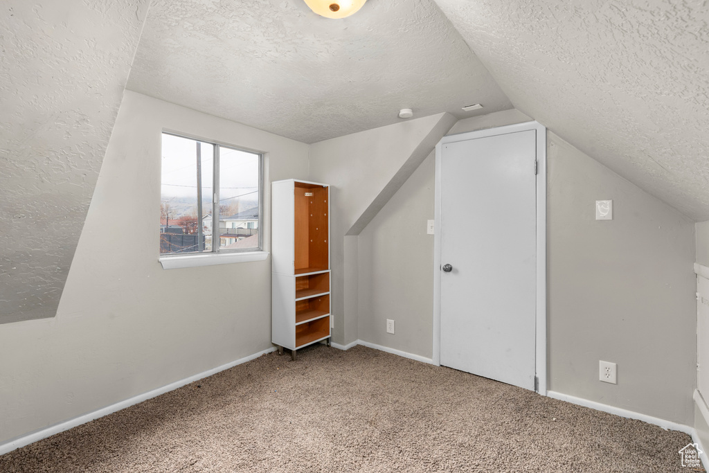 Bonus room with light colored carpet, lofted ceiling, and a textured ceiling
