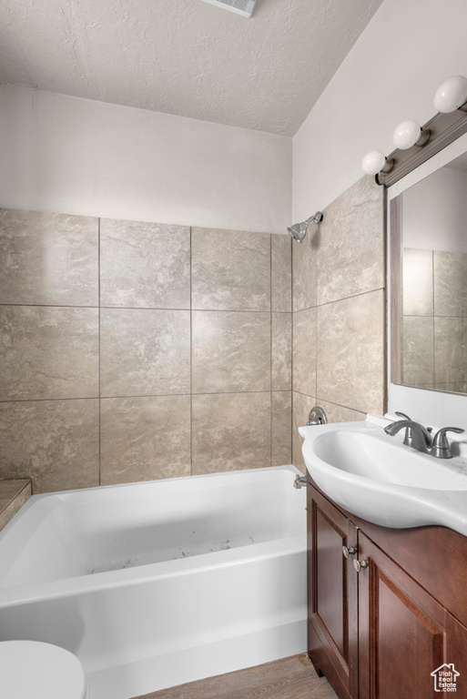 Full bathroom with hardwood / wood-style flooring, a textured ceiling, tiled shower / bath combo, toilet, and vanity