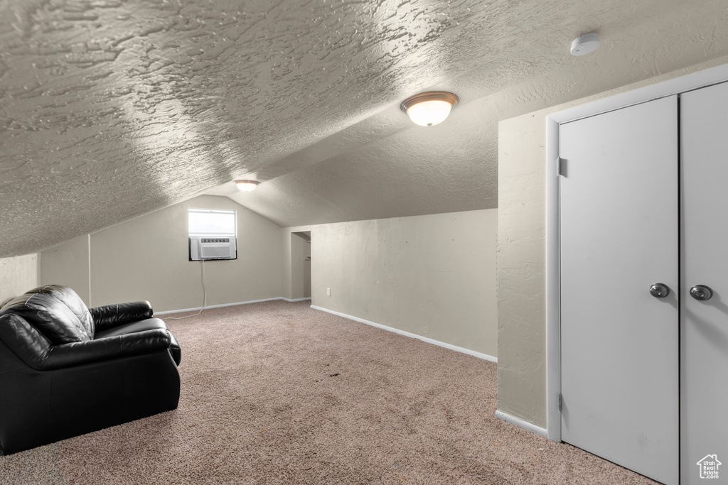 Additional living space featuring light carpet, an AC wall unit, a textured ceiling, and vaulted ceiling