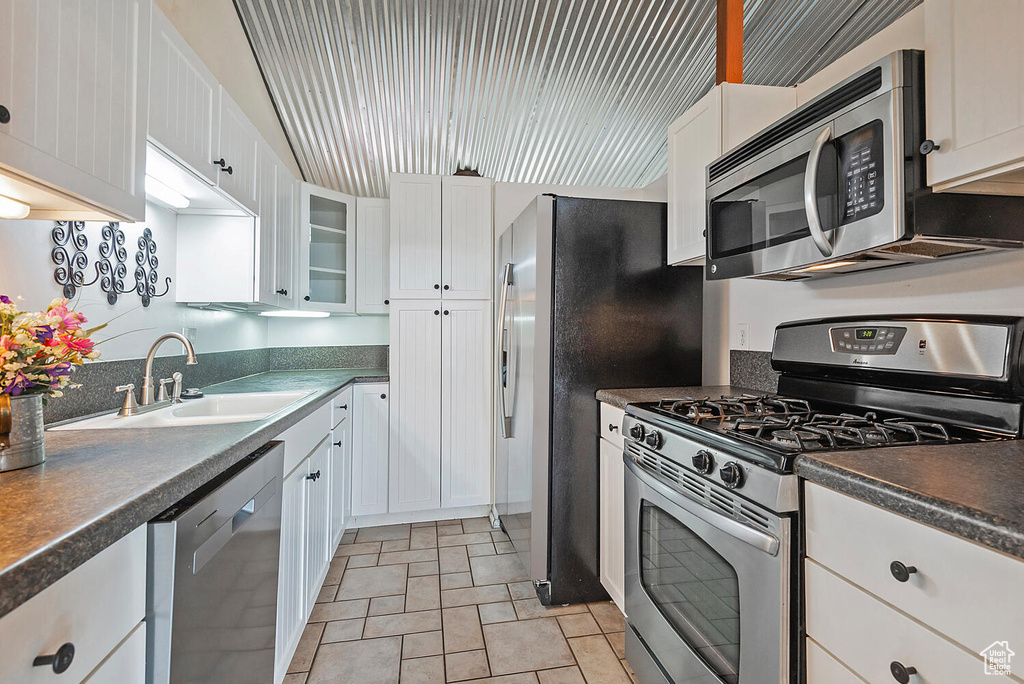 Kitchen featuring appliances with stainless steel finishes, light tile floors, white cabinets, sink, and lofted ceiling
