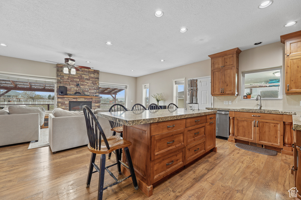 Kitchen featuring a fireplace, a kitchen breakfast bar, light hardwood / wood-style floors, backsplash, and ceiling fan