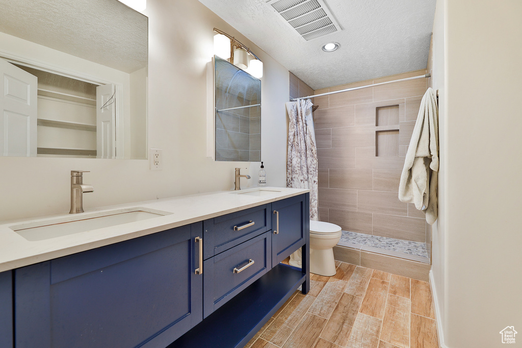 Bathroom with double vanity, toilet, walk in shower, and a textured ceiling