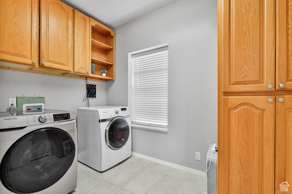 Clothes washing area with independent washer and dryer, light tile floors, hookup for a washing machine, and cabinets