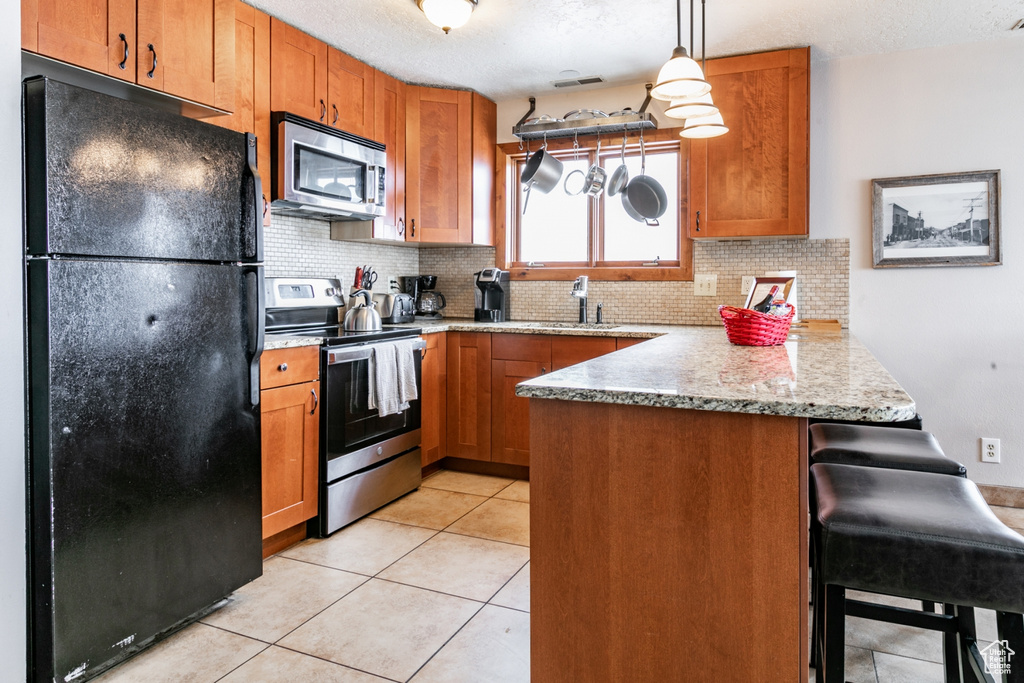 Kitchen featuring appliances with stainless steel finishes, tasteful backsplash, decorative light fixtures, and a breakfast bar