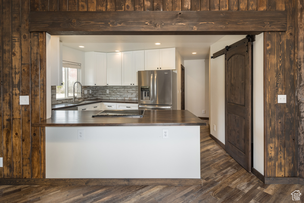 Kitchen featuring backsplash, a barn door, stainless steel appliances, white cabinetry, and dark hardwood / wood-style flooring