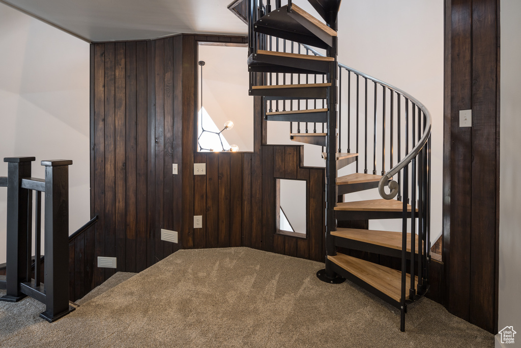 Stairs with a notable chandelier, wood walls, and dark colored carpet