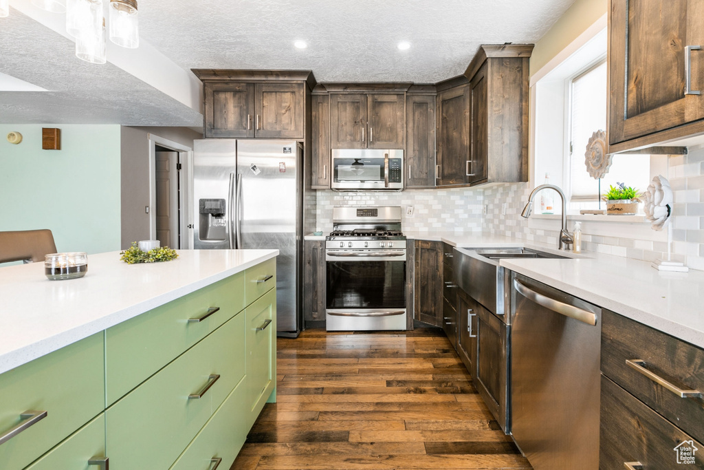 Kitchen featuring tasteful backsplash, dark hardwood / wood-style floors, a textured ceiling, green cabinets, and appliances with stainless steel finishes