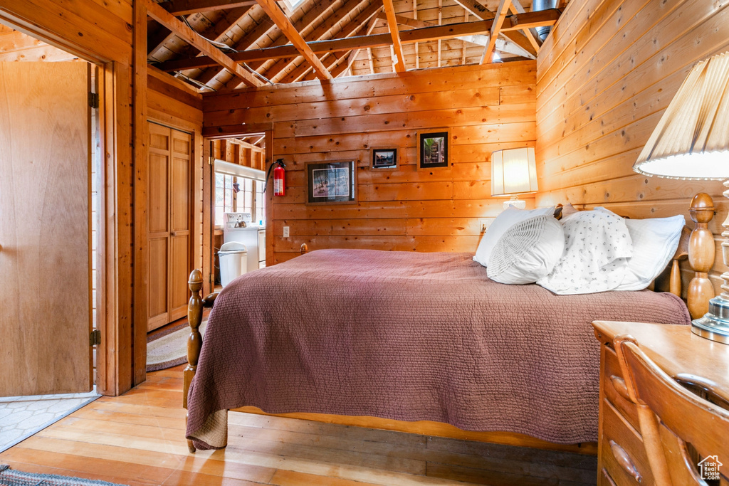 Bedroom with vaulted ceiling with beams, wood walls, ensuite bath, and light hardwood / wood-style floors