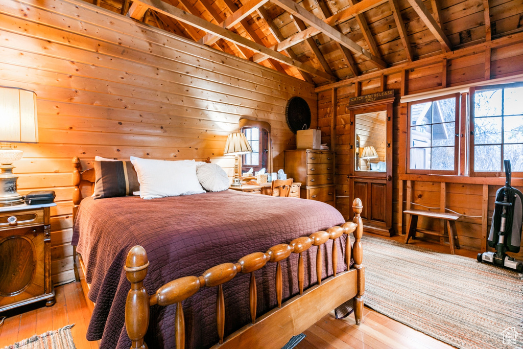 Bedroom with wooden walls, lofted ceiling with beams, light wood-type flooring, and wood ceiling
