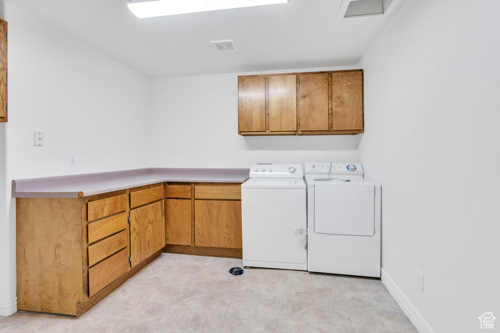 Laundry room featuring separate washer and dryer, light tile floors, and cabinets
