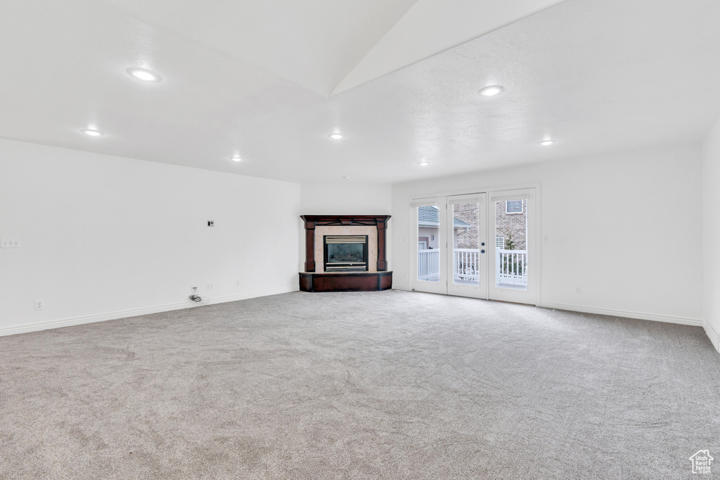 Unfurnished living room with a tile fireplace, lofted ceiling, light colored carpet, and french doors