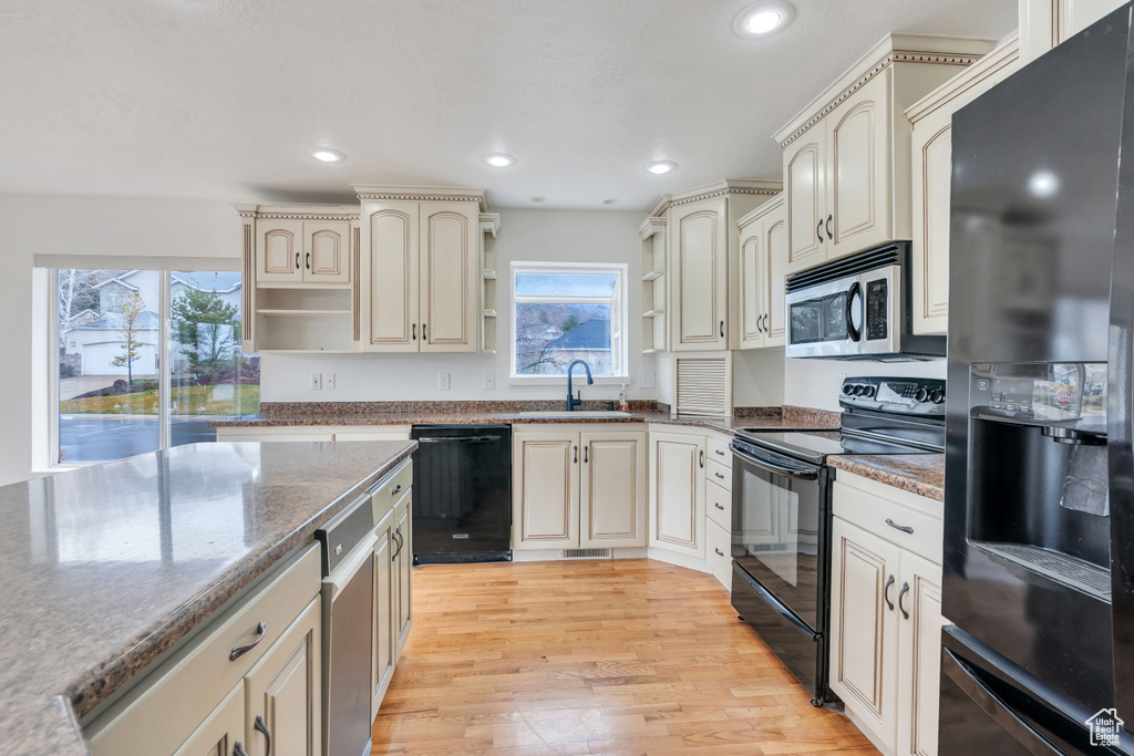 Kitchen with cream cabinetry, light hardwood / wood-style floors, light stone counters, sink, and black appliances