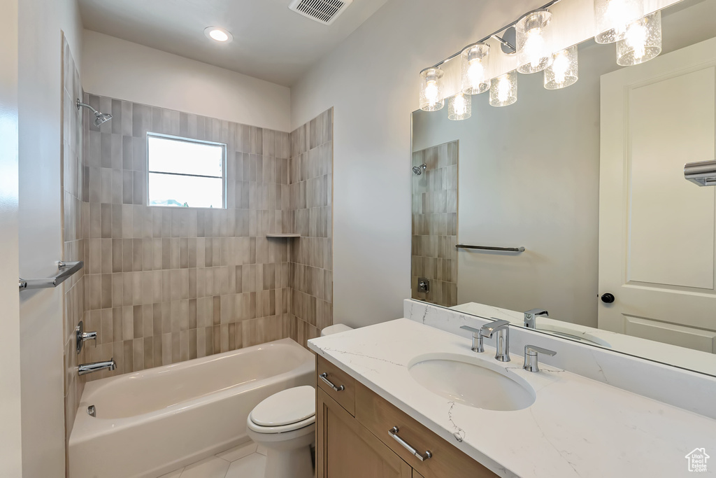 Full bathroom with toilet, tile flooring, vanity with extensive cabinet space, and tiled shower / bath combo