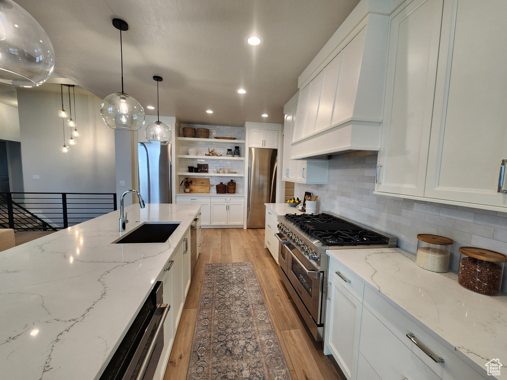 Kitchen with premium range hood, white cabinetry, stainless steel appliances, sink, and tasteful backsplash