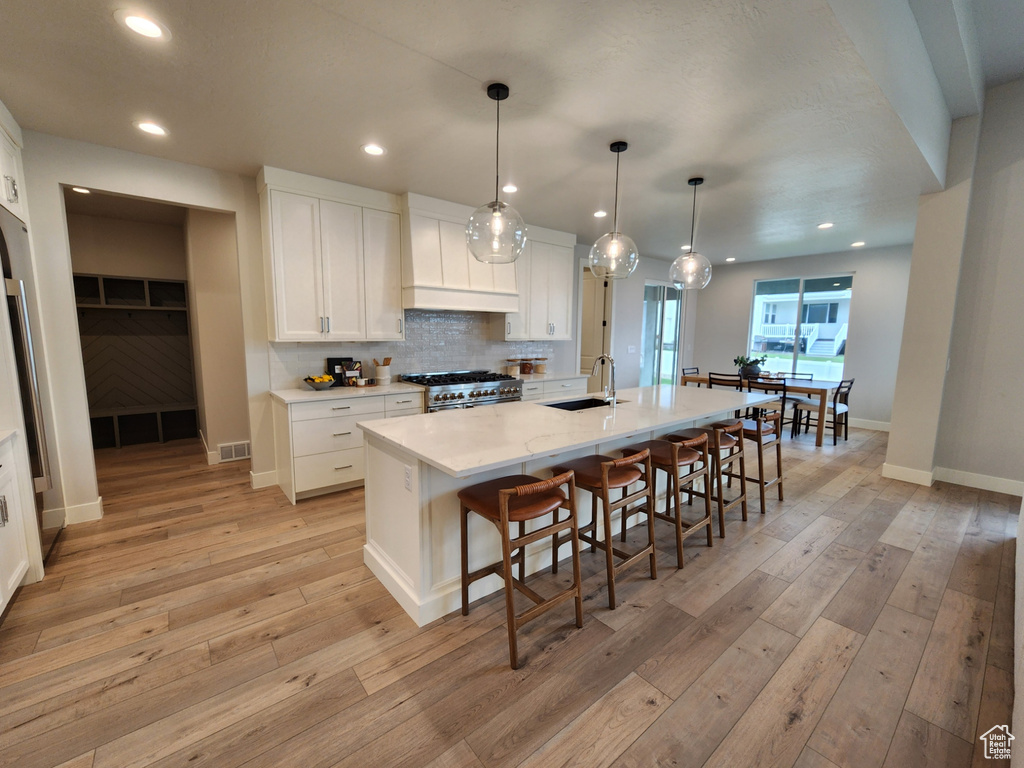 Kitchen featuring white cabinets, light hardwood / wood-style floors, an island with sink, and decorative light fixtures