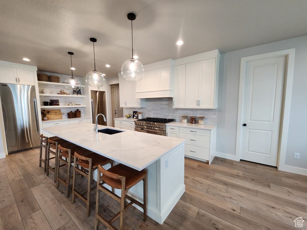 Kitchen featuring white cabinets, sink, appliances with stainless steel finishes, and an island with sink