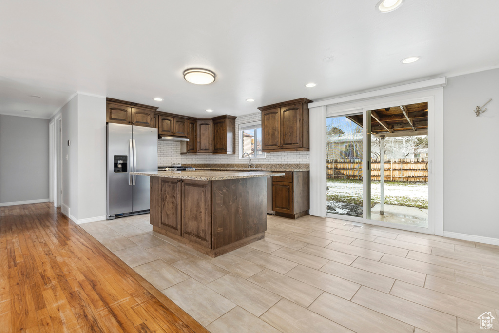 Kitchen featuring light tile flooring, stainless steel refrigerator with ice dispenser, backsplash, a kitchen island, and light stone counters