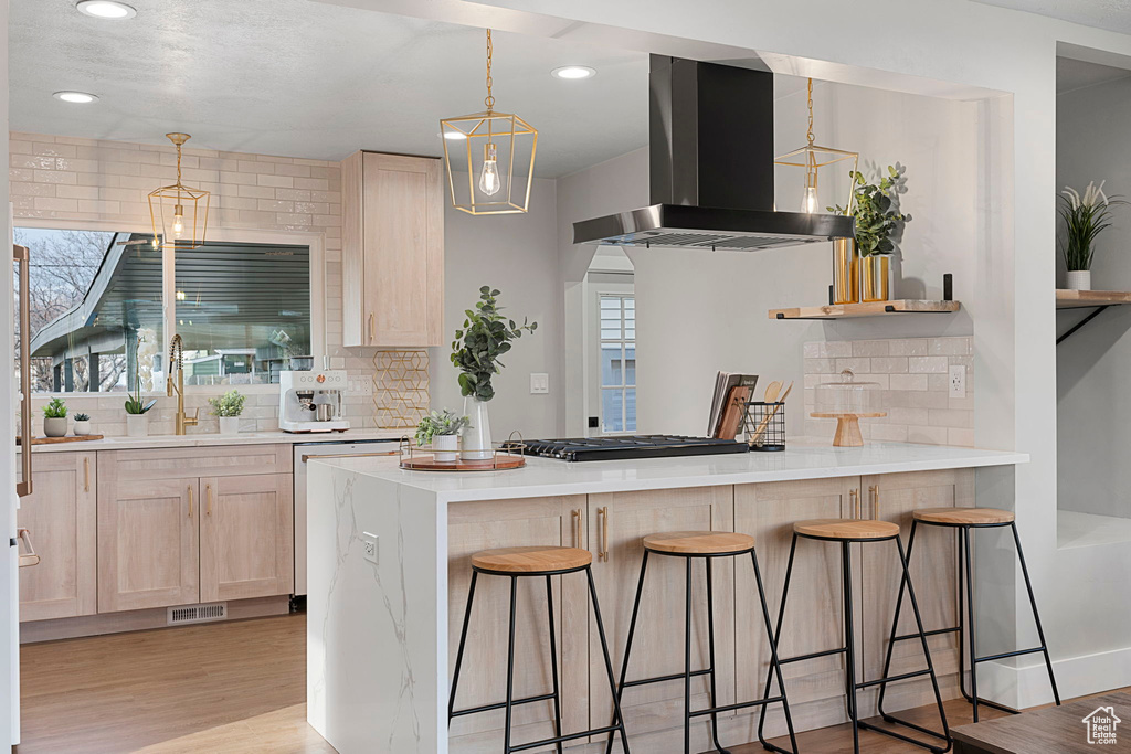 Kitchen featuring tasteful backsplash, decorative light fixtures, light hardwood / wood-style flooring, a kitchen breakfast bar, and fume extractor