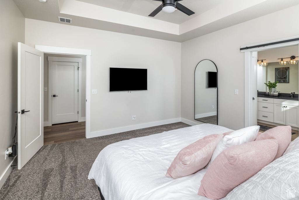 Bedroom with a raised ceiling, ensuite bath, dark carpet, and ceiling fan
