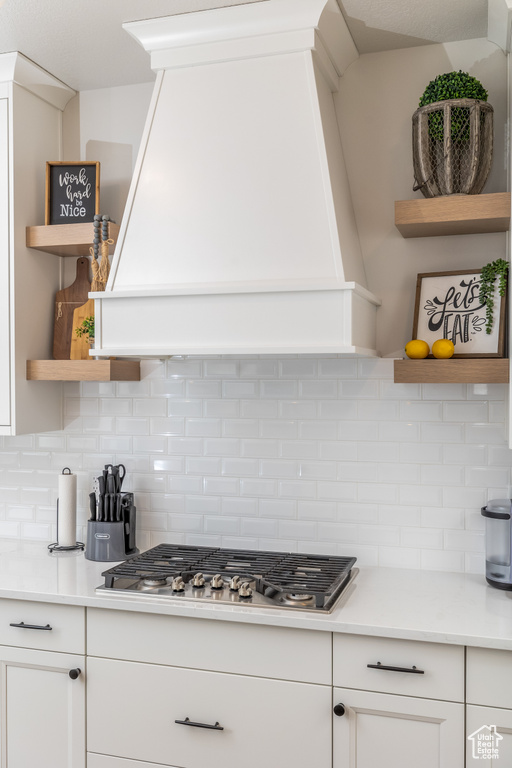 Kitchen featuring custom range hood, white cabinetry, backsplash, and stainless steel gas cooktop