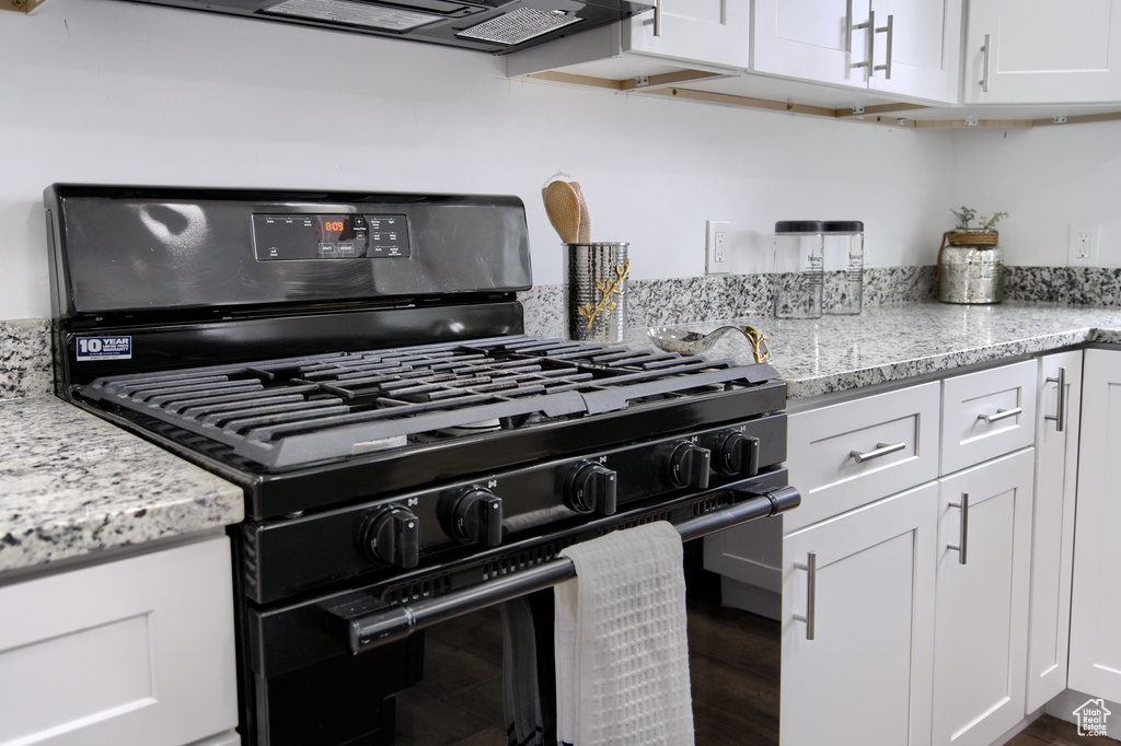 Kitchen featuring white cabinets, light stone counters, and black gas range oven