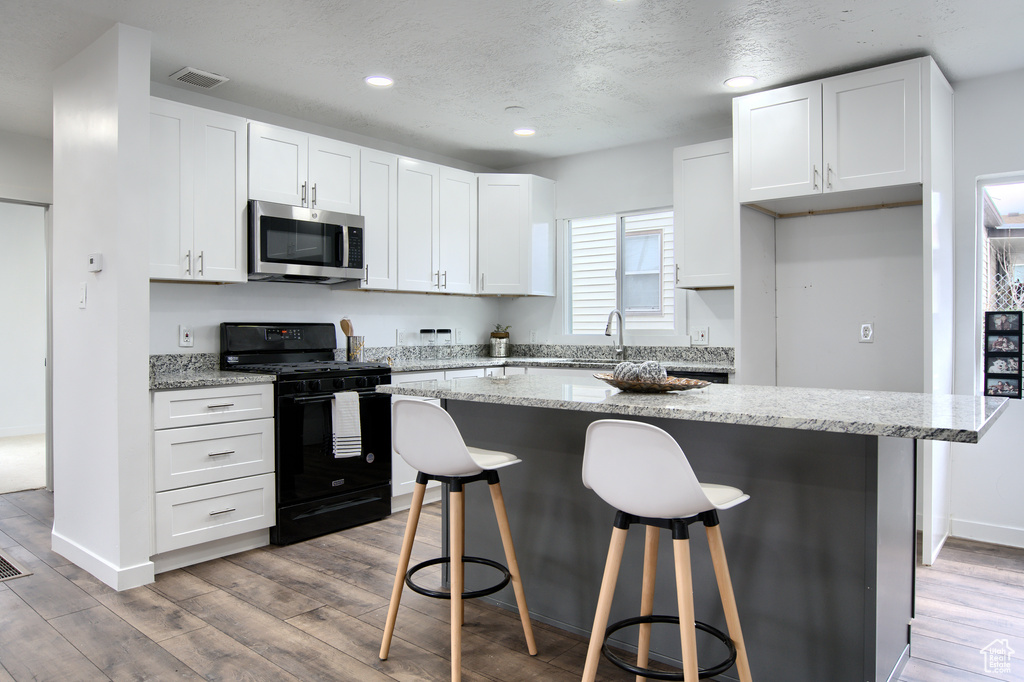 Kitchen featuring white cabinetry, black range oven, a center island, and wood-type flooring
