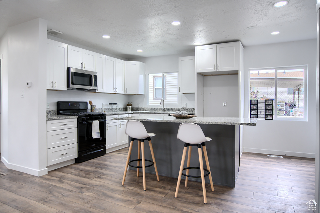 Kitchen featuring black range oven, a kitchen island, white cabinets, and a healthy amount of sunlight