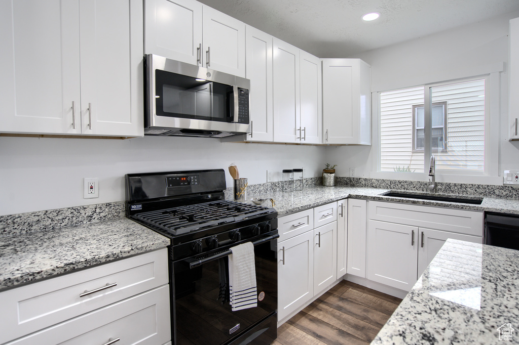 Kitchen featuring black gas range oven, white cabinets, dark hardwood / wood-style floors, and sink