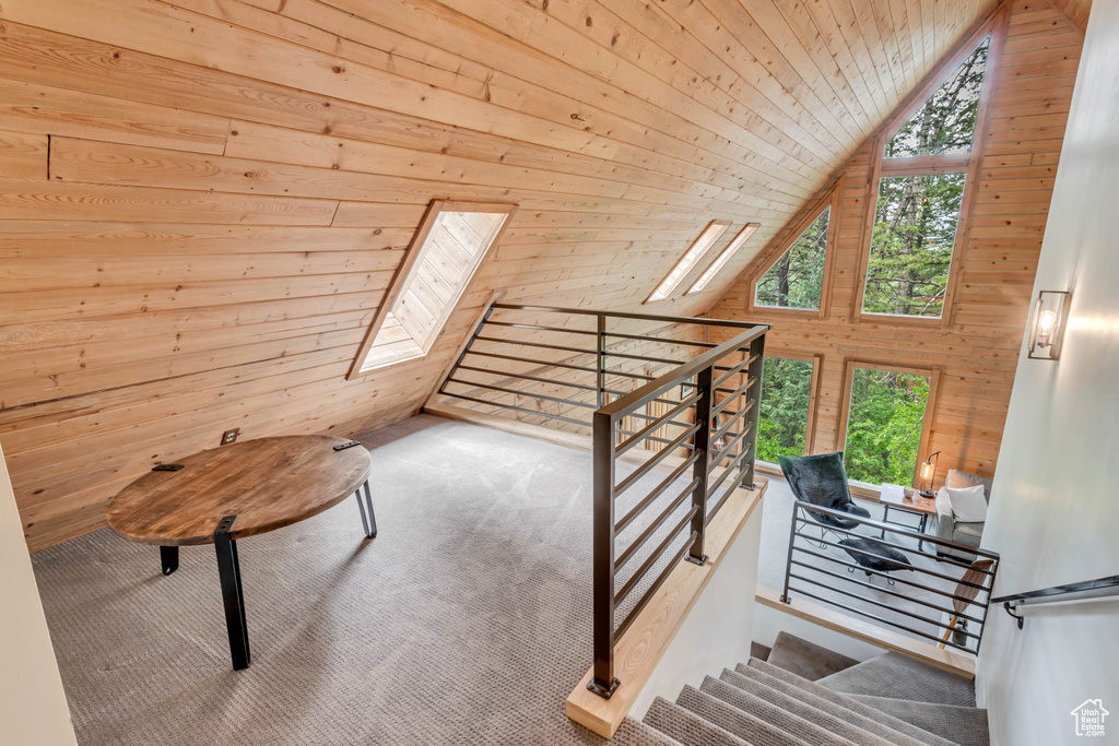 Stairs featuring vaulted ceiling with skylight, wooden walls, wood ceiling, and light colored carpet