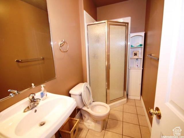 Bathroom with an enclosed shower, toilet, tile flooring, and sink