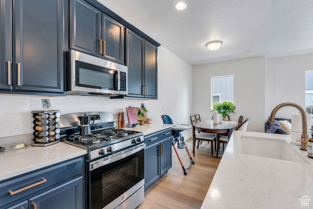 Kitchen featuring stainless steel appliances, sink, light hardwood / wood-style floors, and blue cabinetry