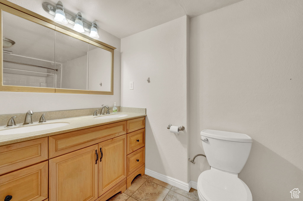 Bathroom with toilet, vanity with extensive cabinet space, tile flooring, and dual sinks