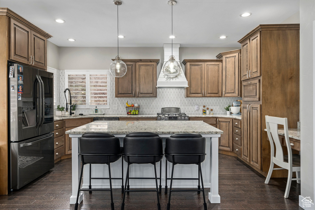 Kitchen featuring dark hardwood / wood-style flooring, light stone countertops, decorative light fixtures, a center island, and stainless steel appliances