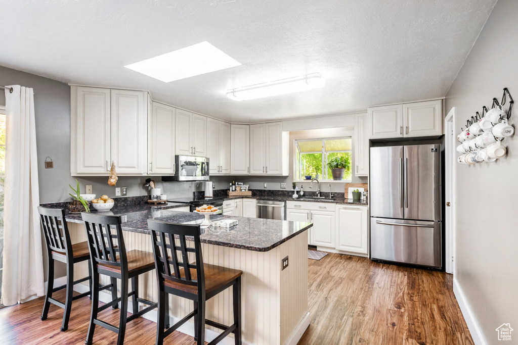 Kitchen featuring a breakfast bar area, white cabinets, stainless steel appliances, and light hardwood / wood-style floors