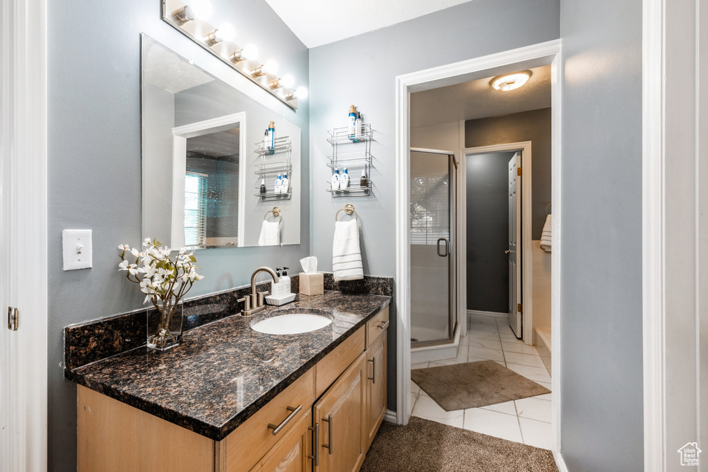 Bathroom with a shower with door, vanity with extensive cabinet space, and tile flooring
