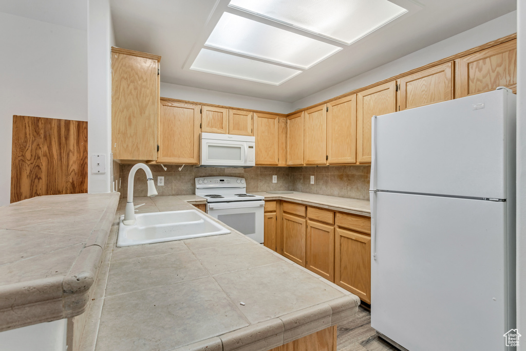Kitchen featuring white appliances, tasteful backsplash, sink, and light brown cabinetry