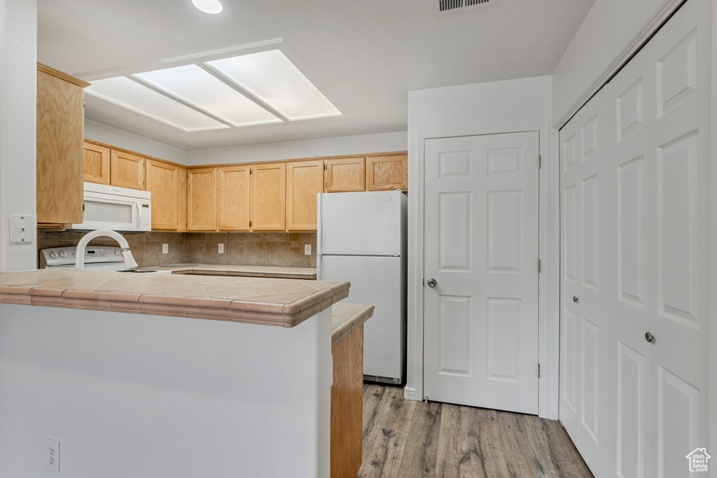 Kitchen featuring white appliances, light wood-type flooring, backsplash, kitchen peninsula, and tile countertops