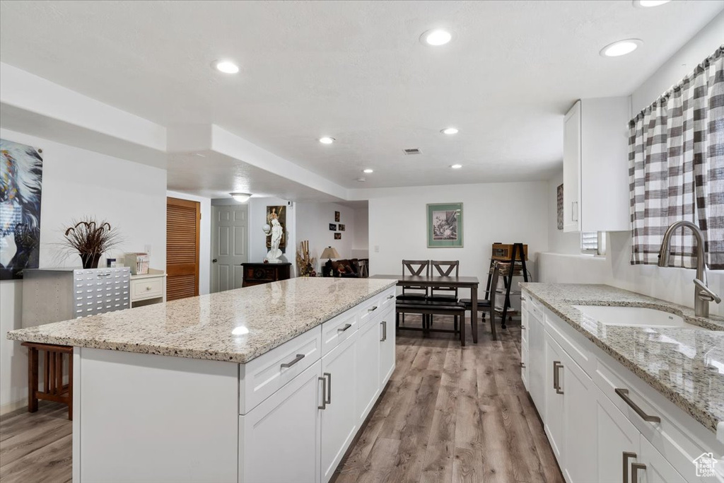 Kitchen with white cabinetry, a center island, sink, light hardwood / wood-style floors, and light stone counters