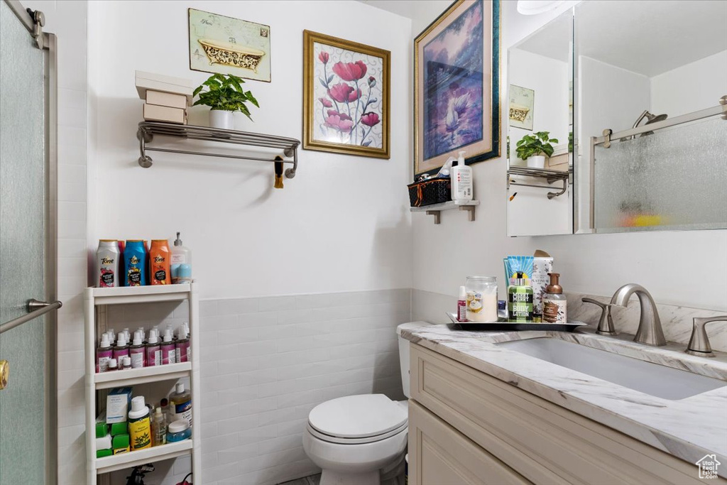 Bathroom featuring vanity, toilet, a shower with door, and tile walls