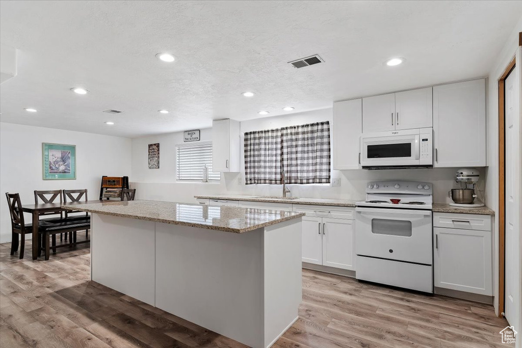 Kitchen with white cabinetry, white appliances, light hardwood / wood-style floors, and a kitchen island
