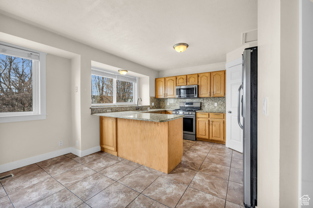 Kitchen featuring appliances with stainless steel finishes, backsplash, light tile flooring, and light stone counters