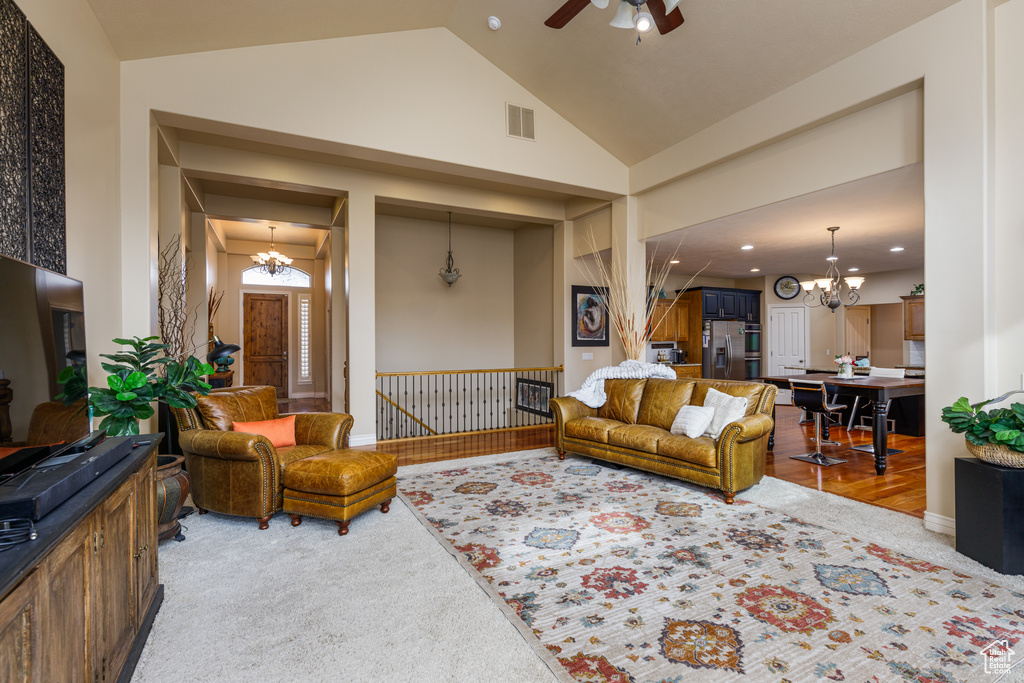 Carpeted living room featuring ceiling fan with notable chandelier and high vaulted ceiling
