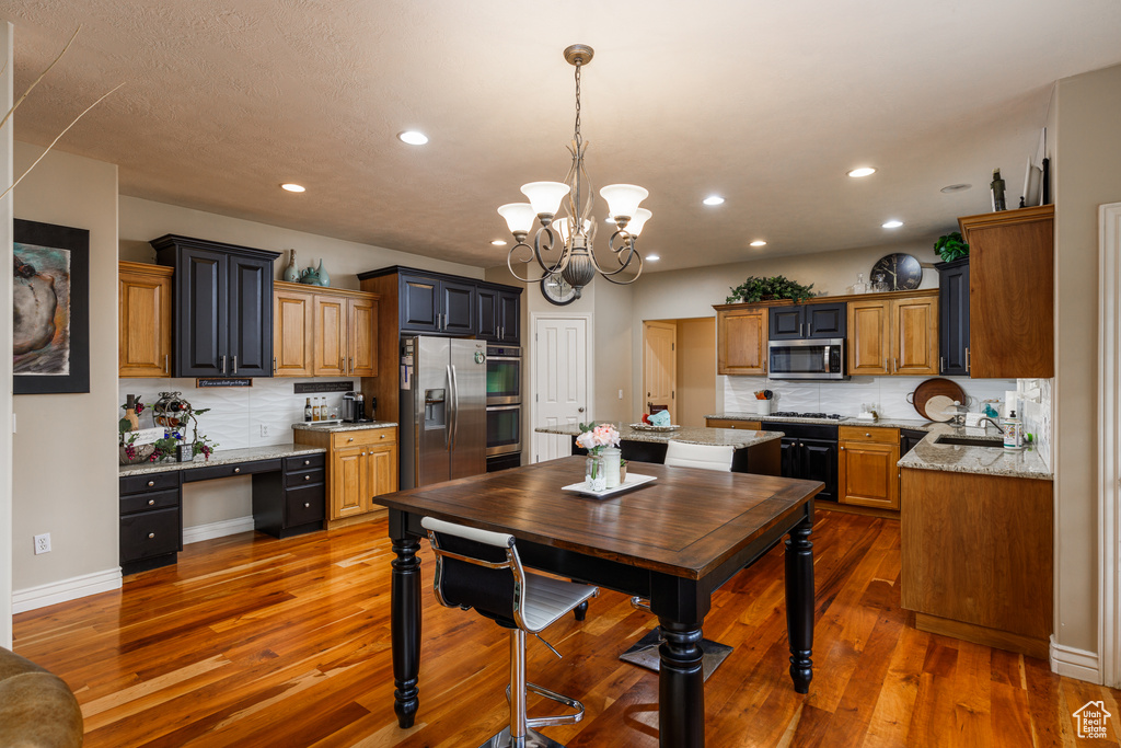Kitchen with tasteful backsplash, hardwood / wood-style floors, a notable chandelier, light stone countertops, and appliances with stainless steel finishes