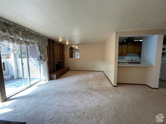 Unfurnished living room with a brick fireplace, light carpet, and a textured ceiling